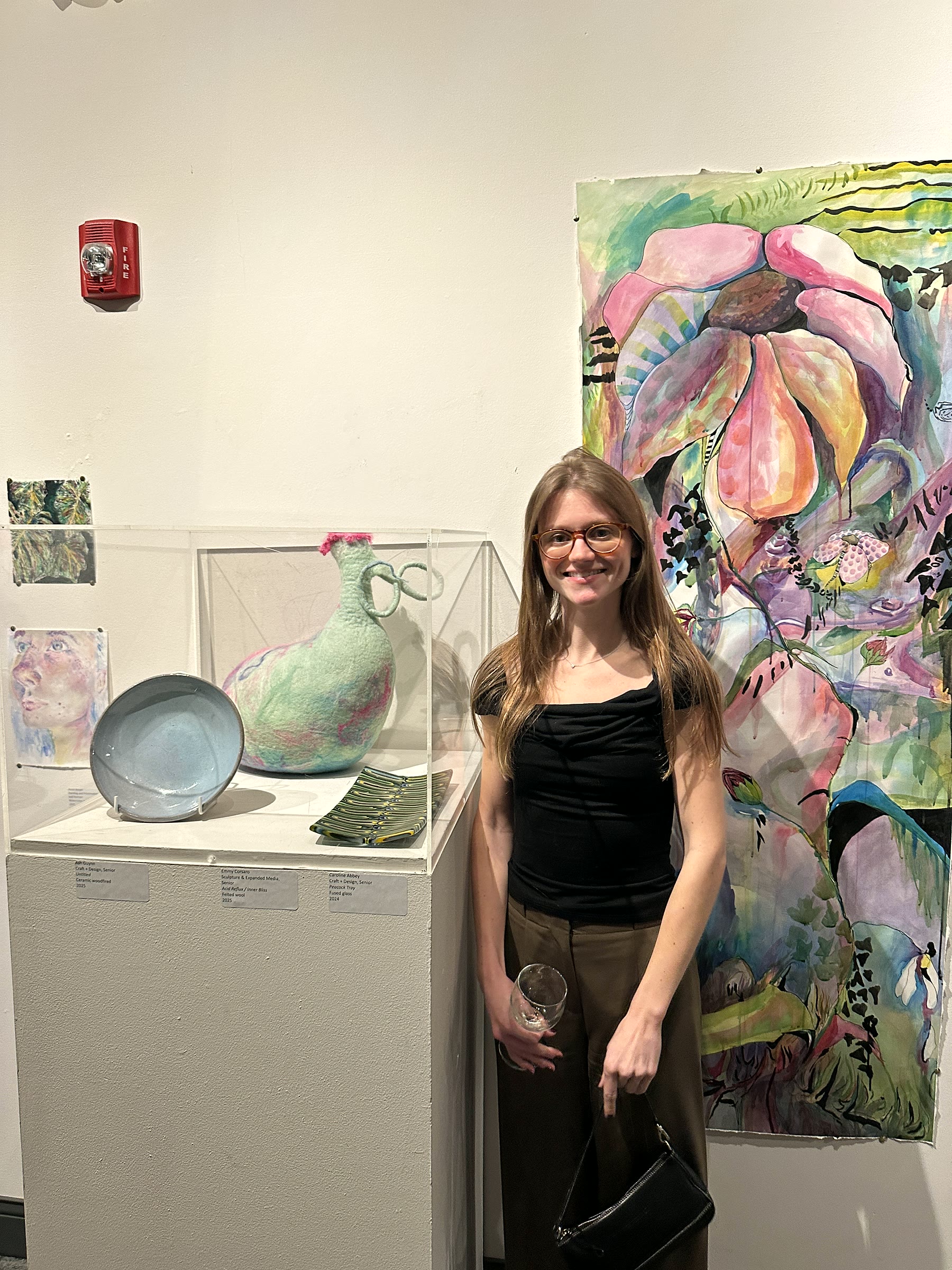 Caroline Abbey standing beside glass works in a gallery exhibition